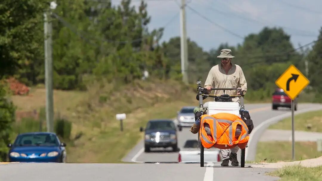 British adventurer Karl Bushby walking through Cameron, North Carolina, pushing pack cart with cars passing by.